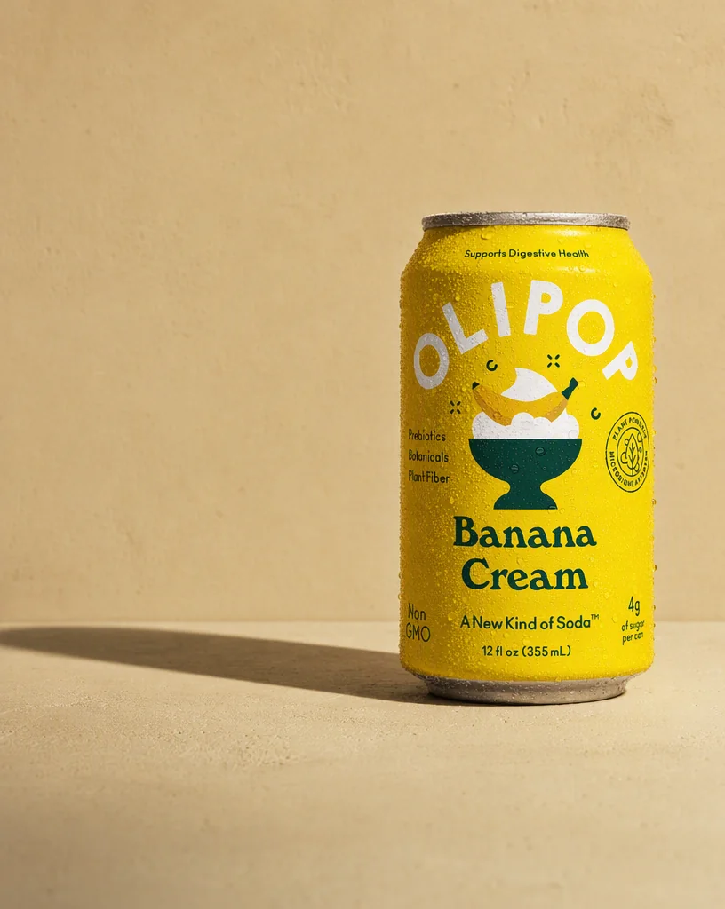 The OLIPOP Banana Cream can on sand toned concrete with a hard diagonal shadow across the wall