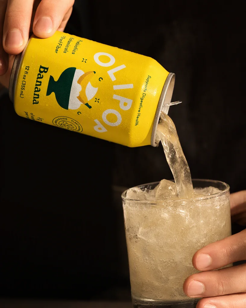 The OLIPOP can pouring into a glass of ice against a dark background