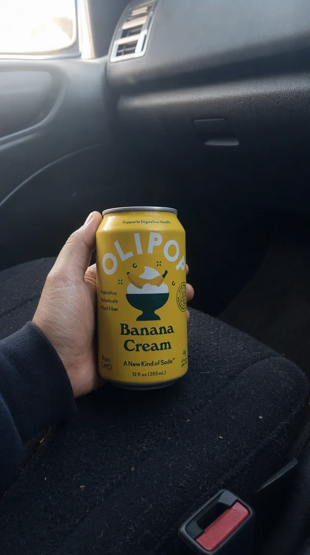 Phone camera style shot of a hand holding the OLIPOP can in a dim parked car